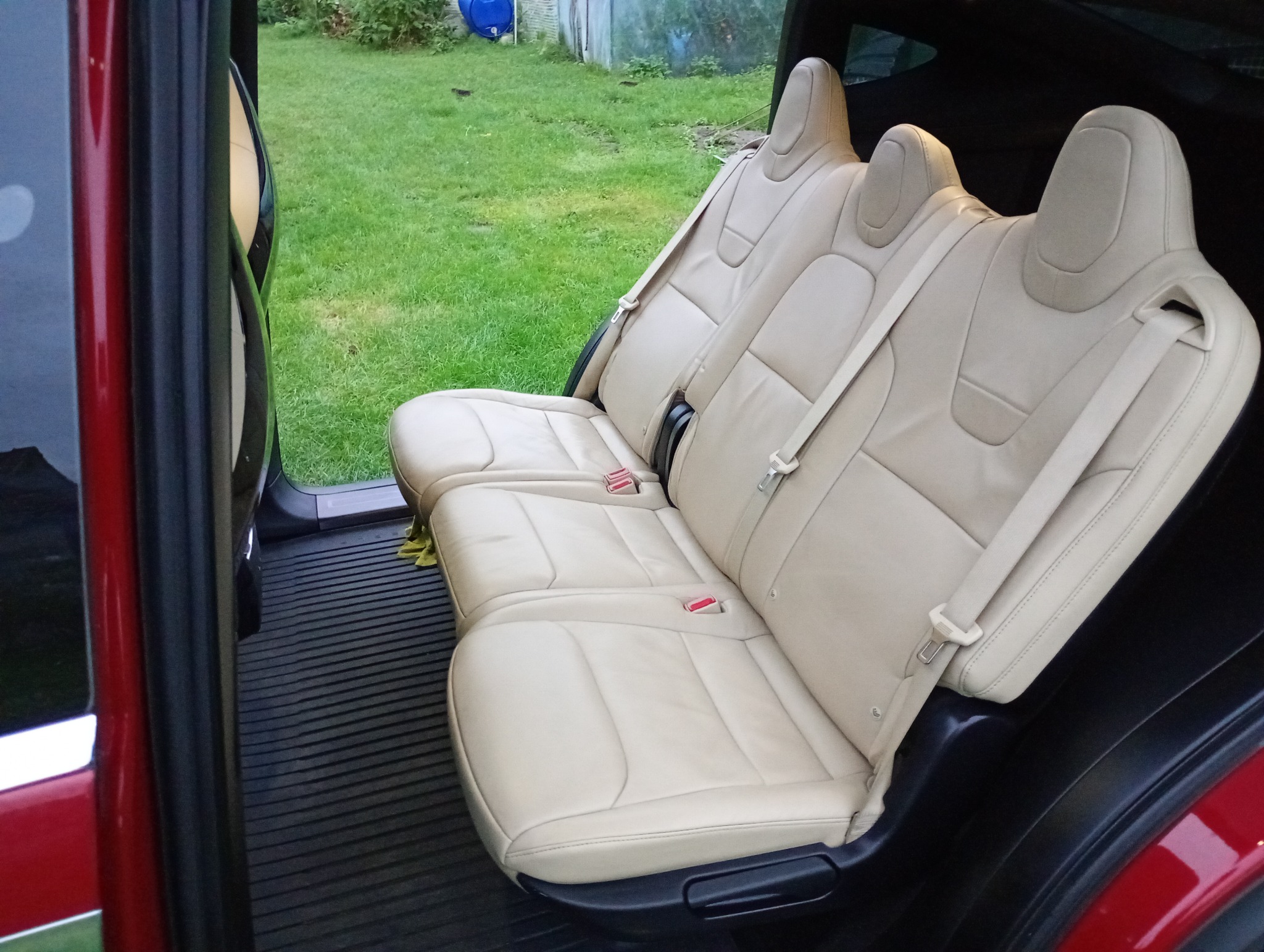 Jasne, skórzane siedzenia drugiego rzędu w samochodzie, widoczne z otwartych drzwi na tle zielonego trawnika.
