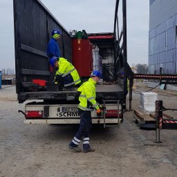 EL-MAR Marek Cegielski - Trzech elektryków w odblaskowych ubraniach wyładowuje z ciężarówki transformator w czerwonej obudowie na palecie, widoczne tablice rejestracyjne WZ 932 SCHMIDT.
