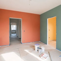 Interiora - Wnętrze po malowaniu ścian na różne kolory (łososiowy, pomarańczowy, zielony, żółty). Na podłodze widoczne farby i wałek malarski. Zabezpieczone taśmą malarską.