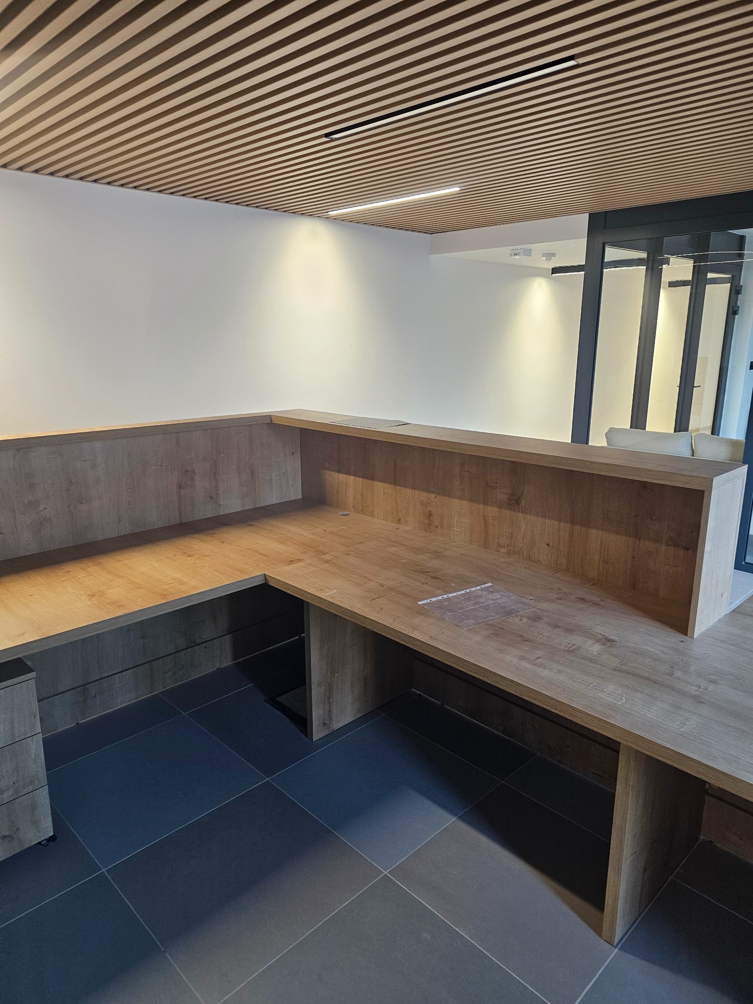 Recepcja biurowa z blatem w kolorze jasnego drewna, widoczne fragmenty zabudowy i sufit z drewnianymi listwami