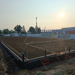 LW CONSTRUCTION S.C. CEZARY WAŚNIEWSKI, KRZYSZTOF LEŚKIEWICZ - Zbrojenie fundamentów pod budowę, widoczne szalunki i siatka z prętów stalowych na tle zachodzącego słońca i przemysłowego krajobrazu.