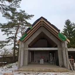 LW Construction s.c. - Surowy stan budynku z betonu komórkowego i drewnianą konstrukcją dachu, widok z zewnątrz w zimowej scenerii. Widoczne bloczki i narzędzia budowlane.