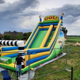 Z.P.U Tapicer - Duża, kolorowa dmuchana zjeżdżalnia z napisem 'GOL!' na tle pochmurnego nieba, z dwójką dzieci i ogrodzeniem.