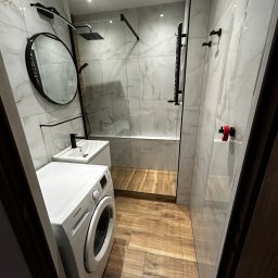 LILAY MONIKA JAKÓBCZYK - Nowoczesna łazienka z kabiną prysznicową typu walk-in, wykończona płytkami imitującymi marmur, drewnopodobną podłogą i czarnymi akcentami armatury, z pralką Samsung w rogu.