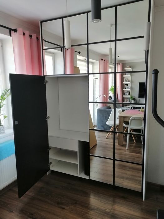 Szafa na wymiar z czarnymi drzwiami i lustrzanymi frontami w stylu loft, widoczna otwarta część z półkami, odbicie wnętrza pokoju w lustrach.