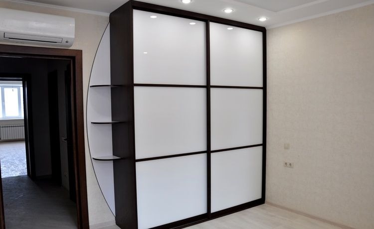 Biała szafa przesuwna z ciemnobrązowymi ramami i półkami bocznymi w minimalistycznym wnętrzu, widok na otwarte drzwi do innego pokoju.