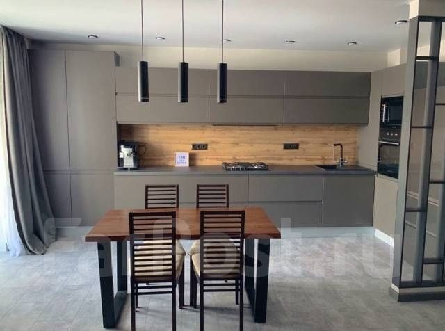 Szara kuchnia z drewnianym blatem i oświetleniem punktowym nad stołem z krzesłami o drewnianej konstrukcji.