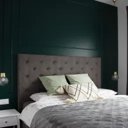 Nowoczesna sypialnia z ciemnozieloną ścianą w panelach, szarym pikowanym zagłówkiem i narzutą, lampkami nocnymi o kulistych kloszach i białą szafką nocną.