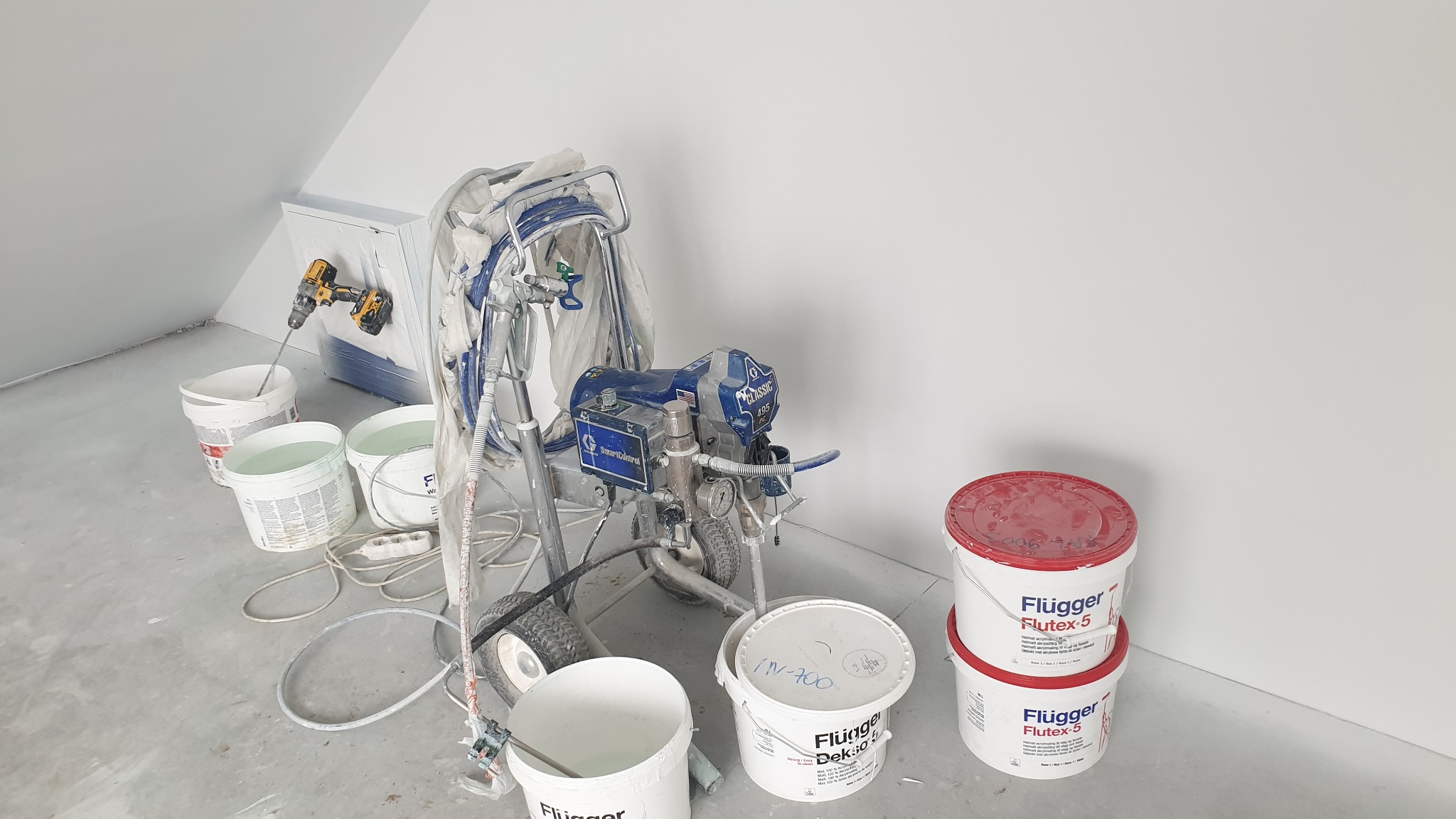 Sprzęt do natryskowego malowania ścian, wiaderka z farbą Flugger, wiertarka z mieszadłem, przygotowania do malowania w pomieszczeniu ze skośnym sufitem.