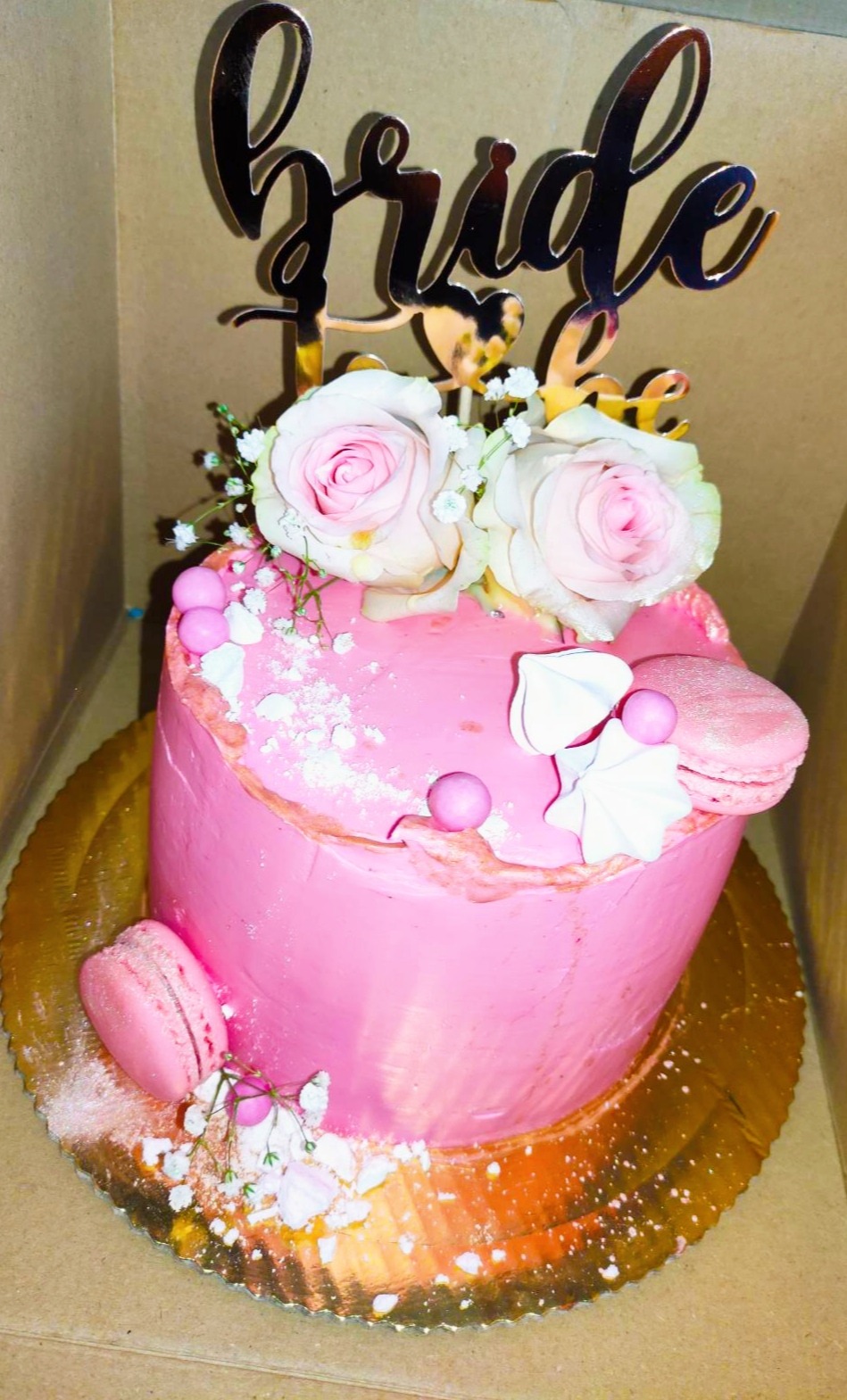 Różowy tort z napisem 'Bride to be', zdobiony różami, bezami i makaronikami, na złotej paterze.