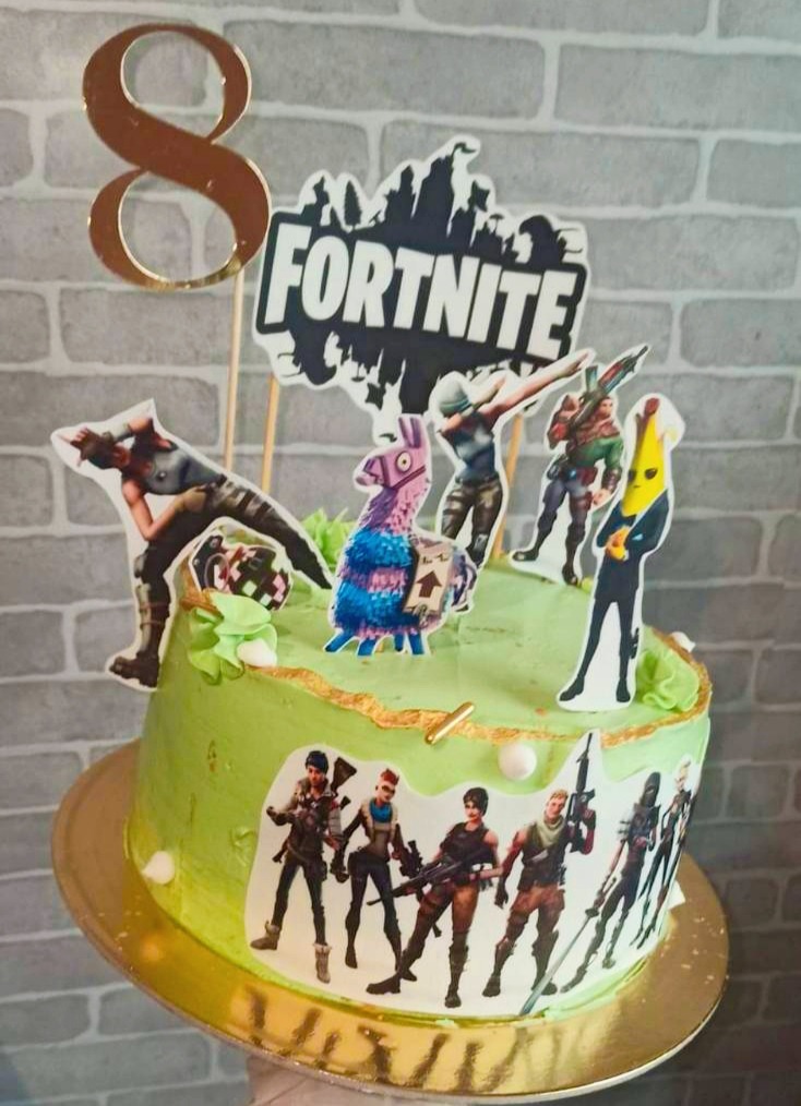Tort urodzinowy z zielonym kremem, dekorowany postaciami z gry Fortnite, numerem 8 na wierzchu i złotymi akcentami, ustawiony na złotej paterze.