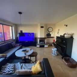 Jasne wnętrze salonu z kremowymi ścianami, ciemnoszarą sofą, fortepianem i kominkiem, po remoncie malarskim.