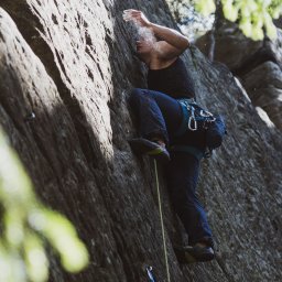 Martyna Kamzol - Wspinaczka skałkowa: kobieta w czarnym topie i jeansach posypuje ręce magnezją, przygotowując się do wspinaczki po skalnej ścianie z liną i uprzężą.