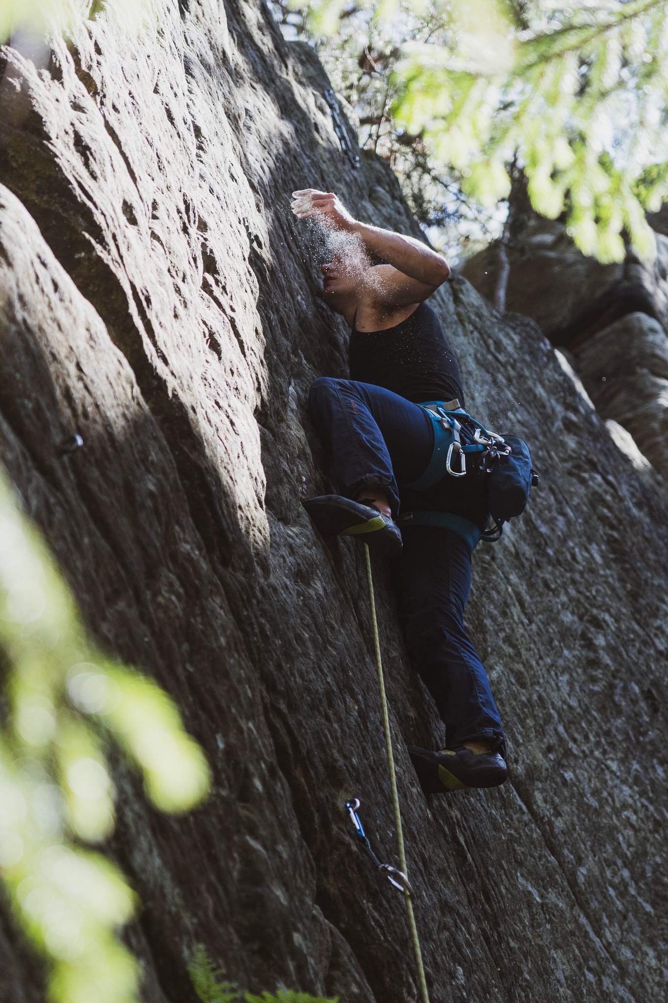 Wspinaczka skałkowa: kobieta w czarnym topie i jeansach posypuje ręce magnezją, przygotowując się do wspinaczki po skalnej ścianie z liną i uprzężą.