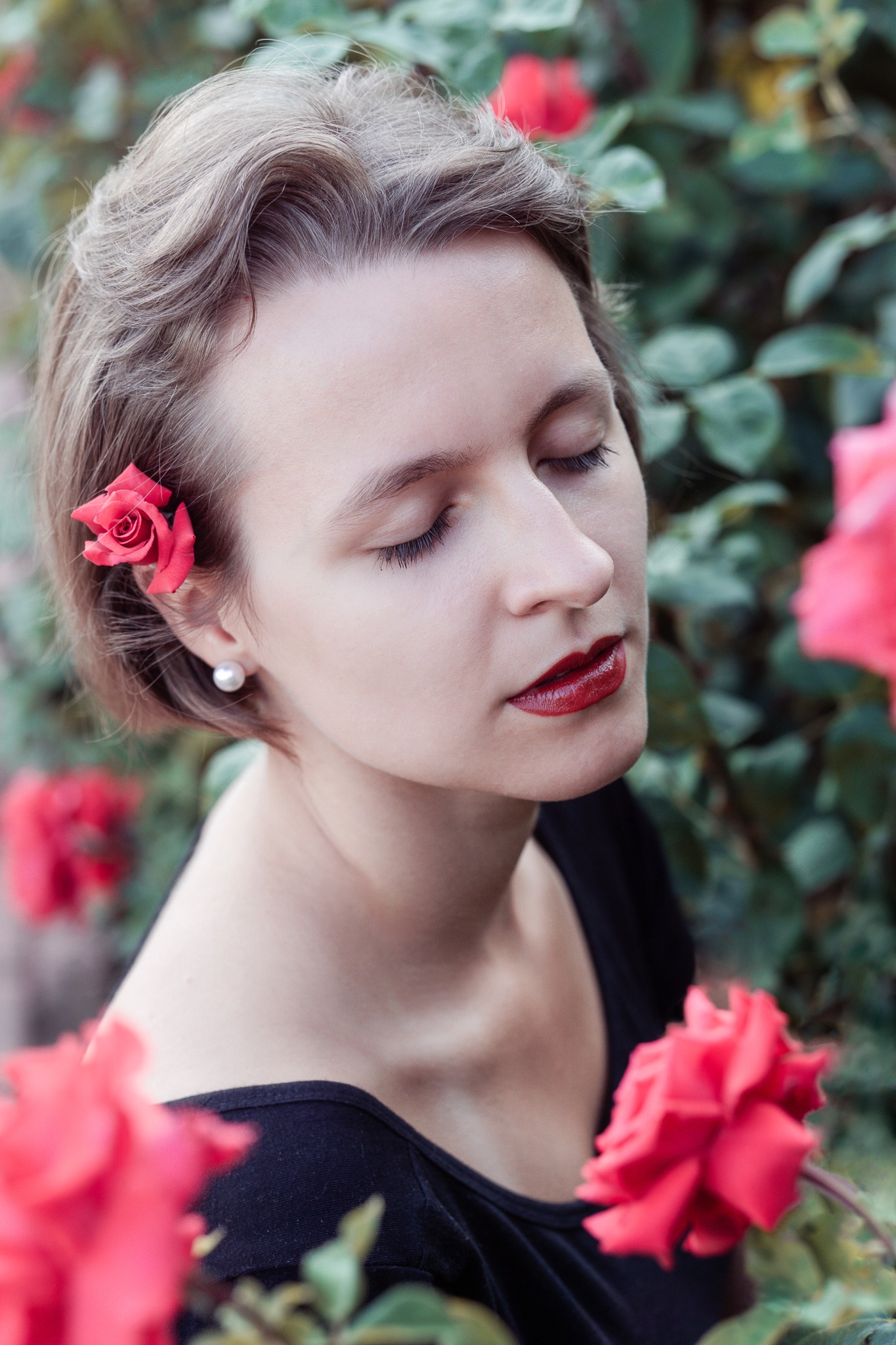 Portret kobiety z zamkniętymi oczami, z różą we włosach i perłą w uchu, otoczonej kwitnącymi różami.