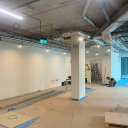Vladyslav Ruban - Prace instalacyjne w nowym lokalu w Krakowie: widoczne koryta kablowe pod sufitem, zamontowane oświetlenie punktowe, pracownicy w kamizelkach odblaskowych oraz przygotowane materiały i narzędzia...