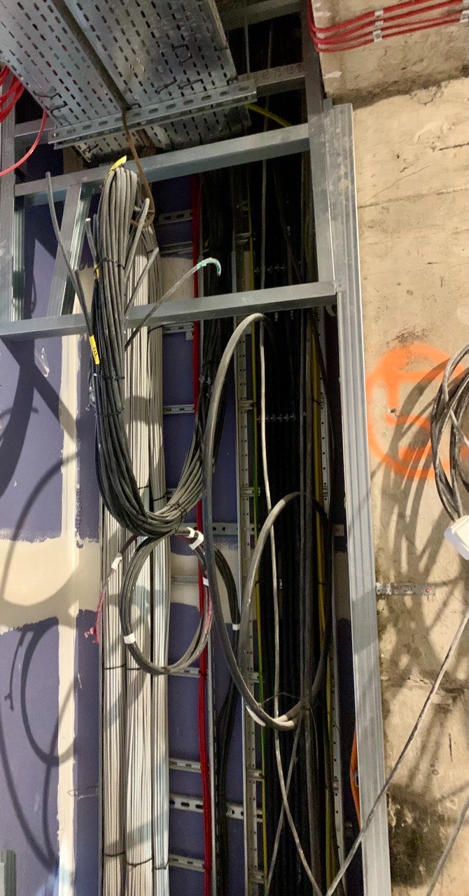 Kłębowisko kabli elektrycznych w metalowej konstrukcji, widoczne przewody różnych kolorów, częściowo zamontowane w ścianie.