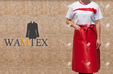 Kobieta w białej koszulce i czerwonym fartuchu z logo firmy na tle ściany imitującej cegły.