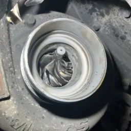 Otwarta turbosprężarka silnika, widoczne łopatki wirnika, zabrudzenia i ślady eksploatacji na obudowie.