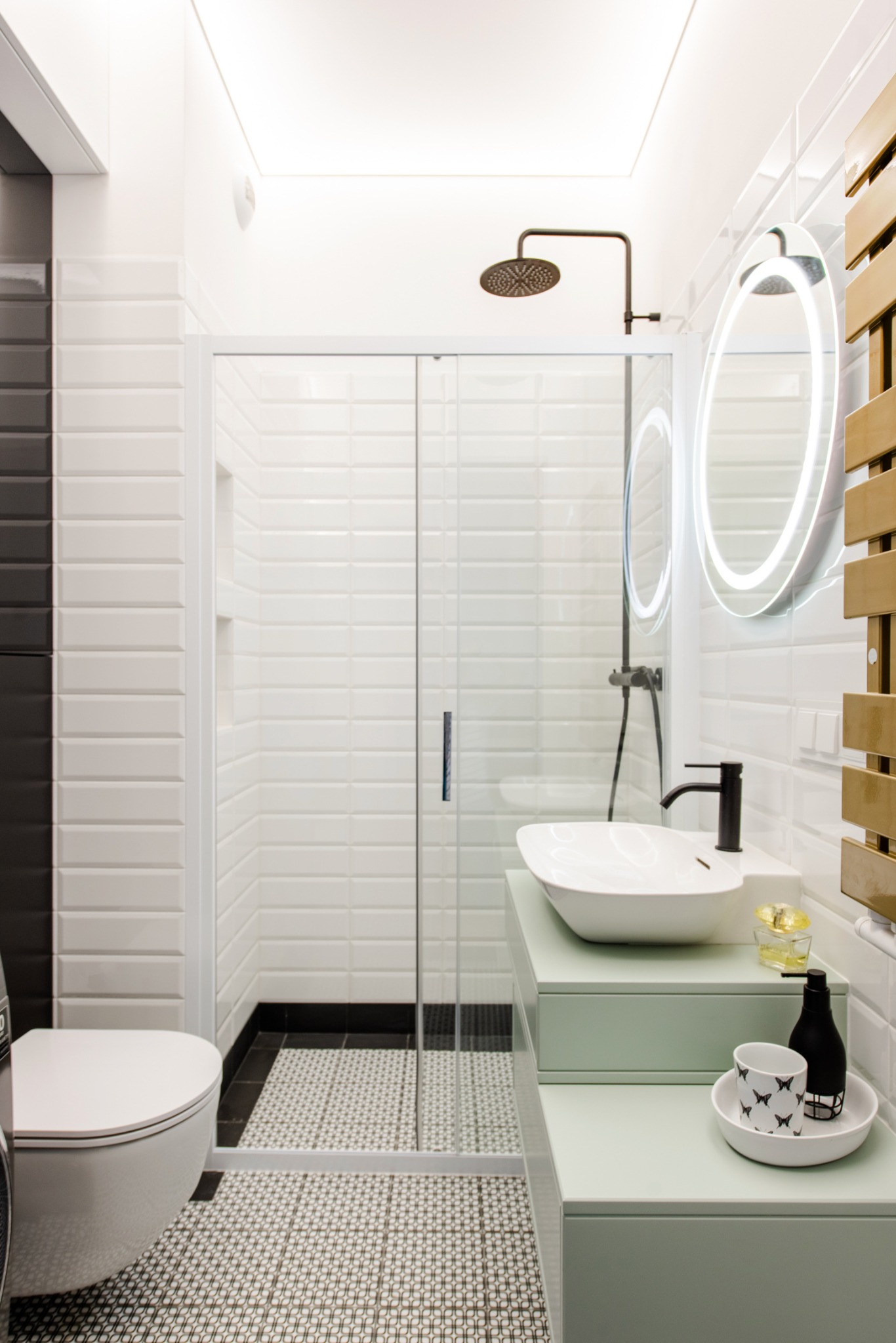 Nowoczesna łazienka z kabiną prysznicową, umywalką na blacie w odcieniu pistacjowym, okrągłym lustrem z podświetleniem LED i mozaikową podłogą.