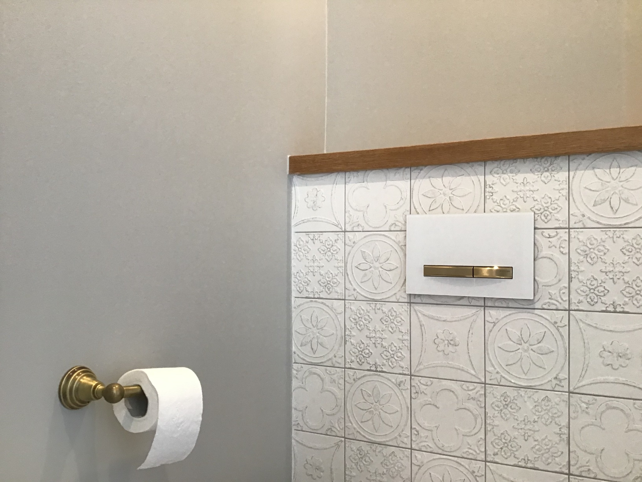 Nowoczesna toaleta z ozdobnymi białymi płytkami, drewnianym blatem i złotym uchwytem na papier toaletowy.