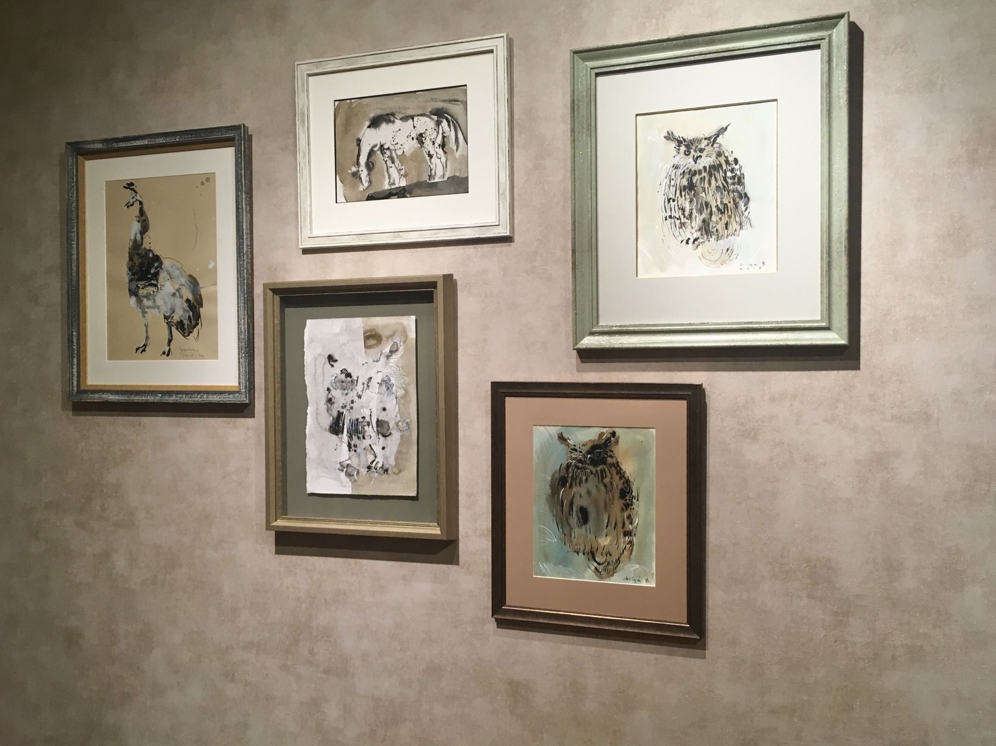 Pięć oprawionych rysunków zwierząt w różnych stylach, wiszących na teksturowanej, beżowej ścianie.