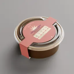 Zamknięte, okrągłe opakowanie z brązowego kartonu z przezroczystą pokrywką, zawierające hummus ze szparagami 'San Comida', z etykietą w pastelowych odcieniach różu, prezentowane na jednolitym...