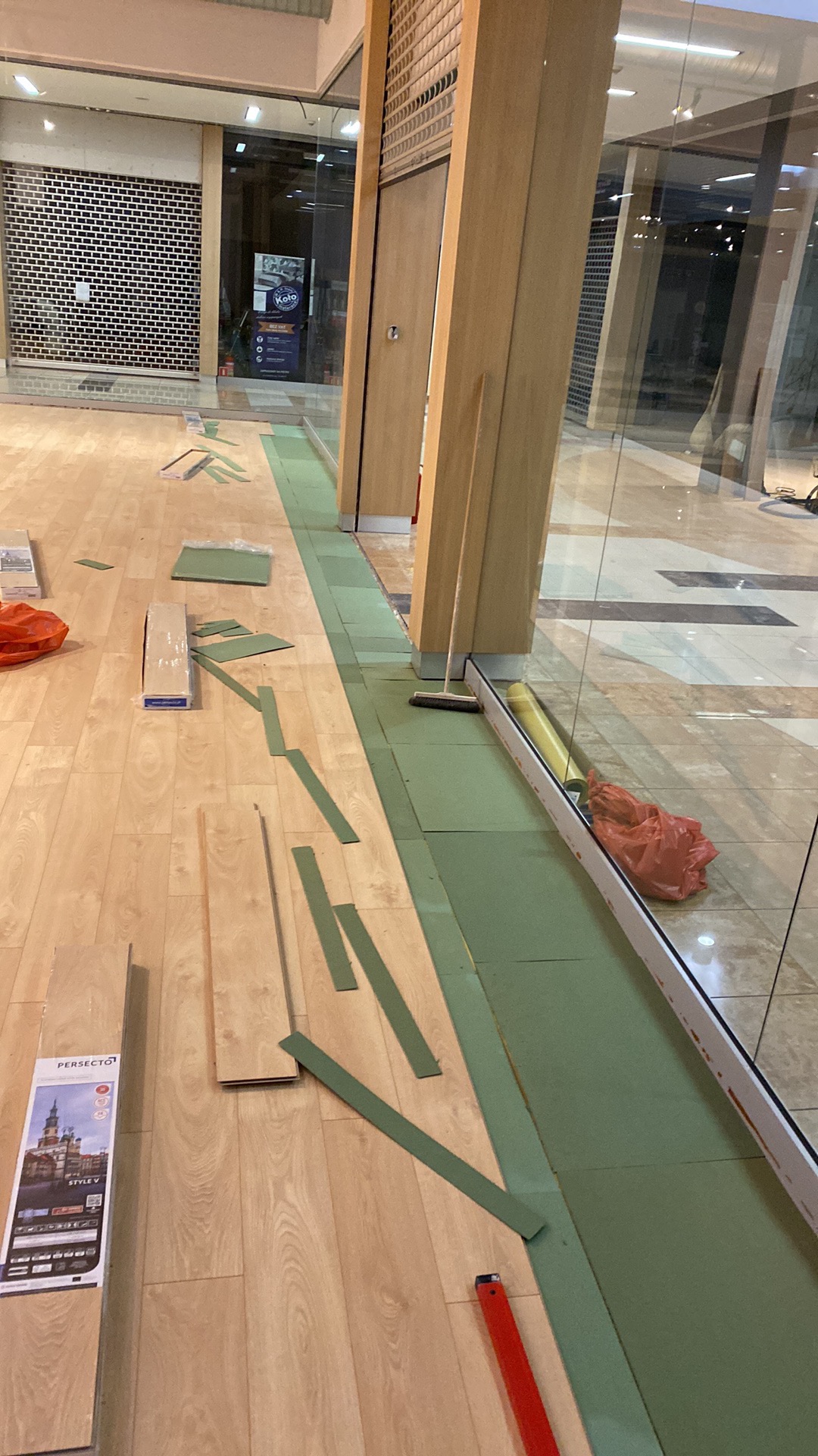 Podłoga w trakcie montażu paneli w lokalu handlowym, widoczne panele, podkład, listwy, narzędzia i instrukcja montażu.