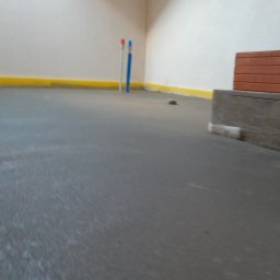 Technobud Henryk Wziątek - Świeżo wylana, szara posadzka jastrychowa w pomieszczeniu z białymi ścianami i żółtą listwą przypodłogową, widoczne wystające rury instalacji oraz cegły i deski tworzące prowizoryczną konstrukcję.