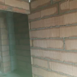 Wnętrze budynku w trakcie budowy, widoczne ściany z pustaków ceramicznych, spoiny z zaprawy, oraz otwór drzwiowy w stanie surowym.