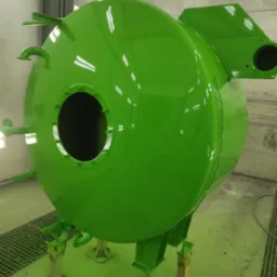 Jasnozielona, pomalowana kula z metalowymi elementami na zewnątrz, umieszczona na stojakach w lakierni.