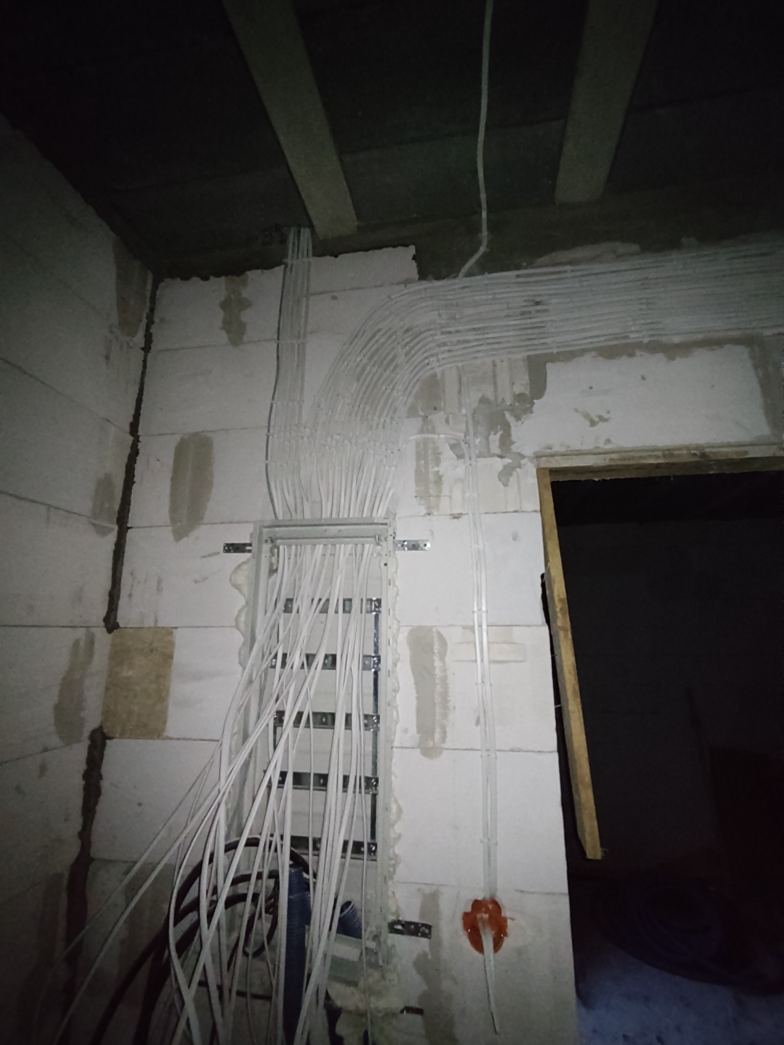 Rozprowadzenie przewodów elektrycznych w białych peszlach na ścianie z betonu komórkowego w trakcie prac instalacyjnych, widoczna puszka instalacyjna i skrzynka rozdzielcza.