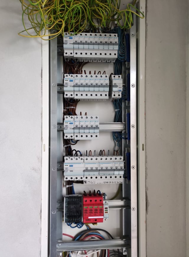 Rozdzielnica elektryczna z widocznymi zabezpieczeniami nadprądowymi, ogranicznikami przepięć, przewodami i elementami montażowymi, z nieułożonymi przewodami u góry.