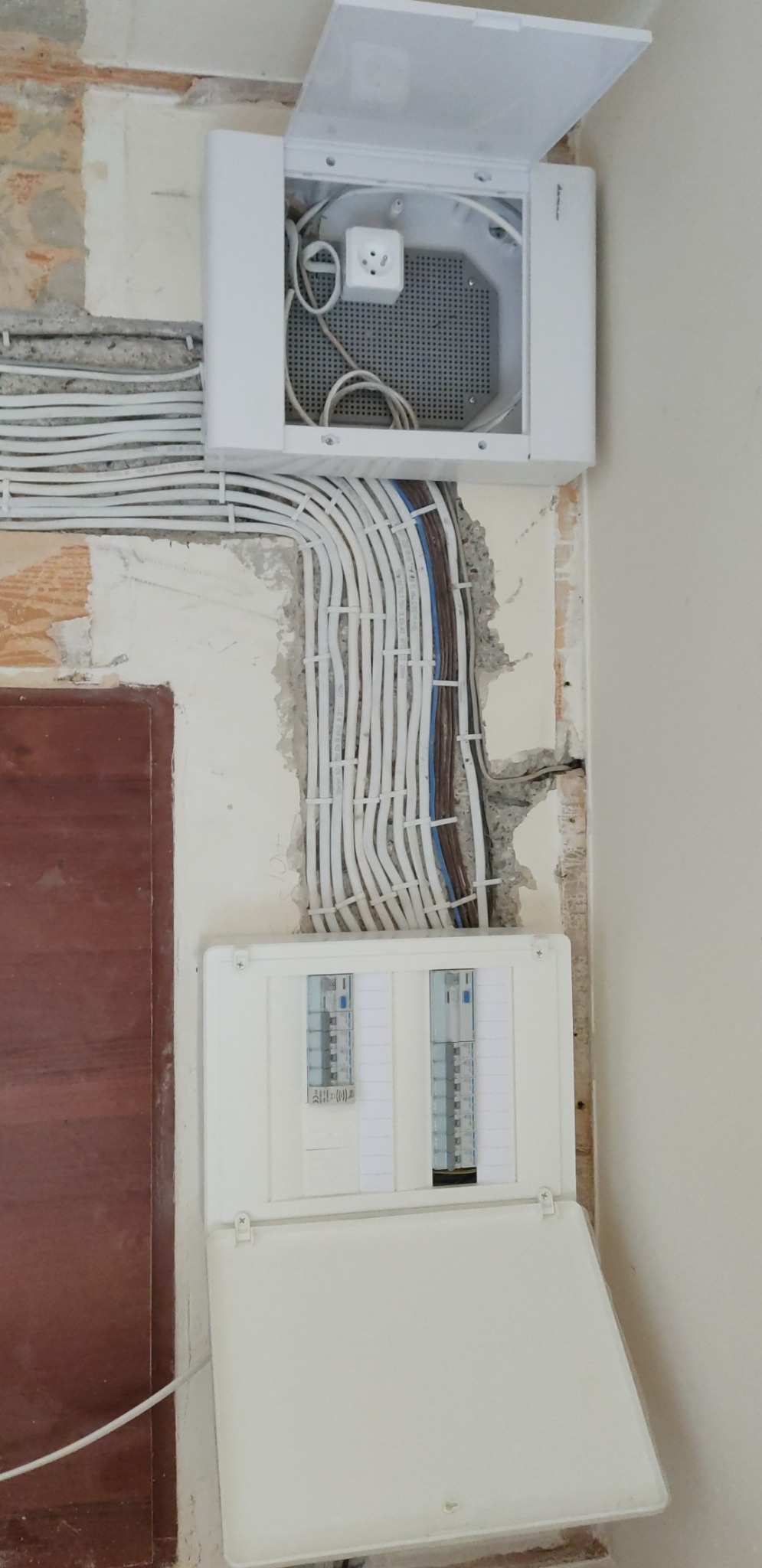 Rozdzielnica elektryczna z otwartą pokrywą, widoczne liczne kable elektryczne ułożone w ścianie, gniazdko w puszce instalacyjnej