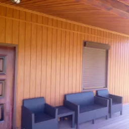 Zadaszony taras z brązową boazerią, zamkniętą roletą okienną i zestawem mebli ogrodowych z rattanu w kolorze grafitowym.