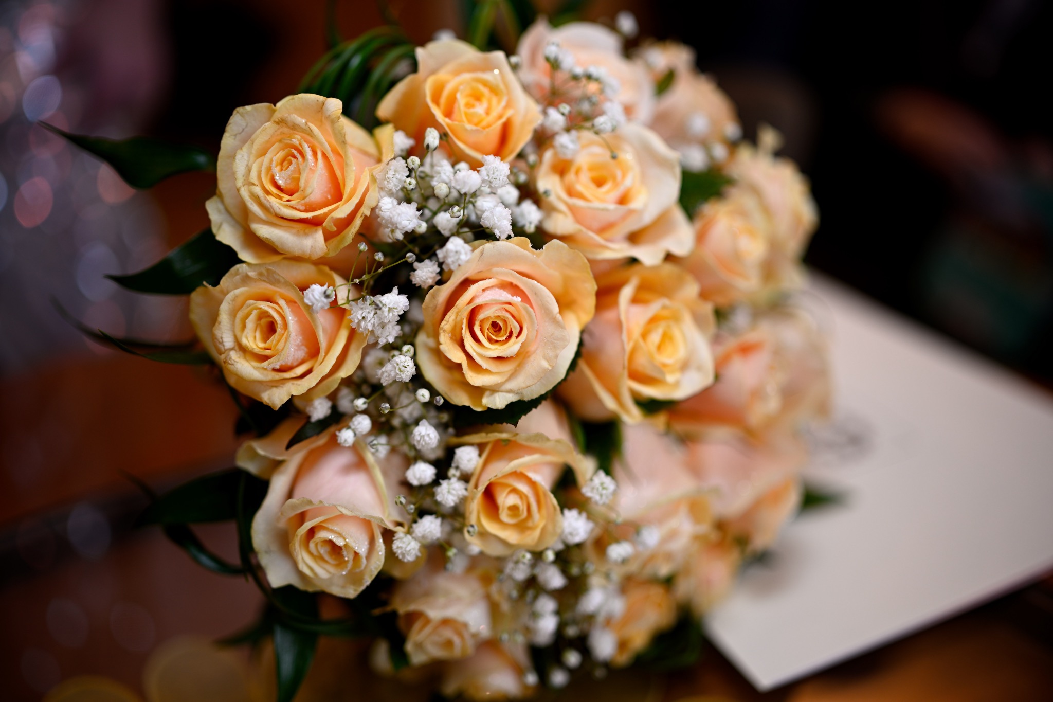 Bukiet ślubny z herbacianych róż i gipsówki, delikatne krople wody na płatkach, ułożony na białym dokumencie.