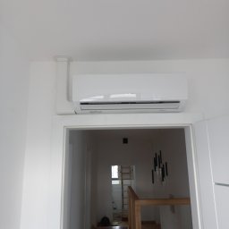Termserwis Jacek Sapak - Biały klimatyzator zamontowany nad framugą drzwi w jasnym wnętrzu, widoczna instalacja odprowadzająca skropliny, w tle schody i drabina.