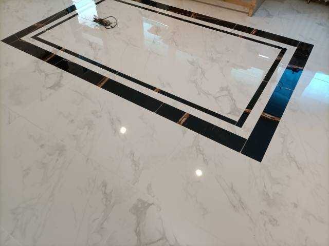 Wykończona podłoga z białych, marmurkowych płytek z dekoracyjnym, prostokątnym obramowaniem z ciemnych płytek.