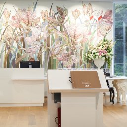 Szymon Skibiński - Wnętrze salonu z recepcją i ekspozycją tapet z motywem kwiatowym, widoczne biurko z komputerem, katalog tapet oraz dekoracja kwiatowa w wazonie.