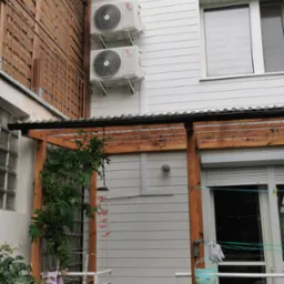 Dwa białe klimatyzatory na elewacji domu z drewnianą pergolą i elementami dekoracyjnymi na balkonie.