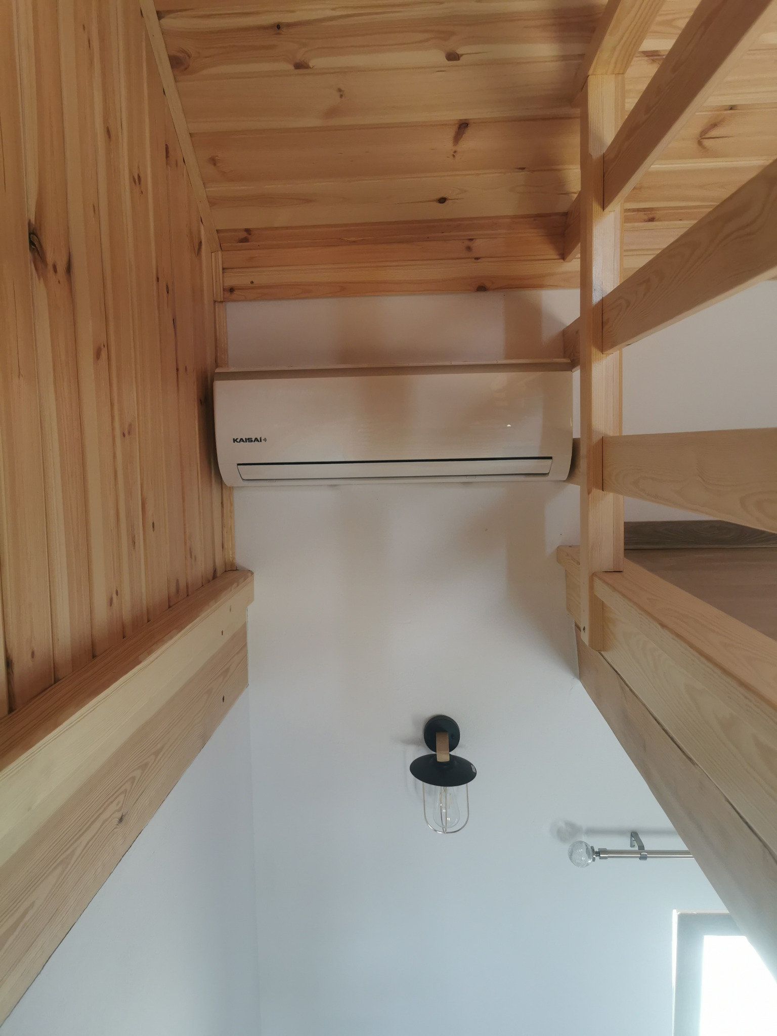 Klimatyzator Kaisai zamontowany w pomieszczeniu z drewnianym stropem i schodami, widoczna lampa w stylu industrialnym.