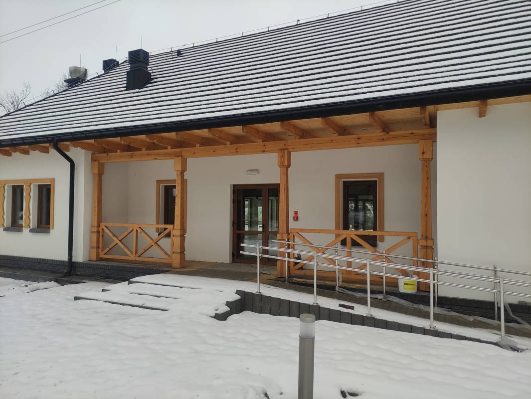 Nowo wybudowana remiza strażacka w Rataju Ordynackim z drewnianą werandą, podjazd dla niepełnosprawnych i fragmentem ośnieżonego terenu.