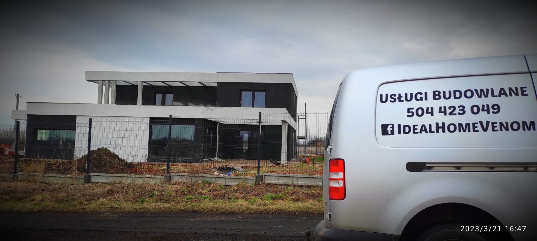 Nowoczesny dom w trakcie budowy, widoczny zza srebrnego samochodu dostawczego z napisem 'Usługi Budowlane' i danymi kontaktowymi firmy.