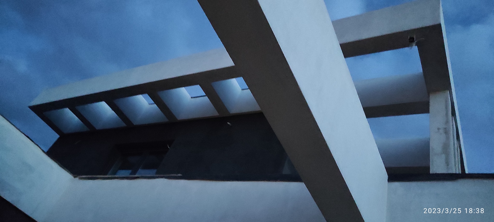 Surowy stan konstrukcji domu z widocznymi betonowymi belkami i otworami okiennymi, sfotografowany pod kątem w pochmurny dzień.