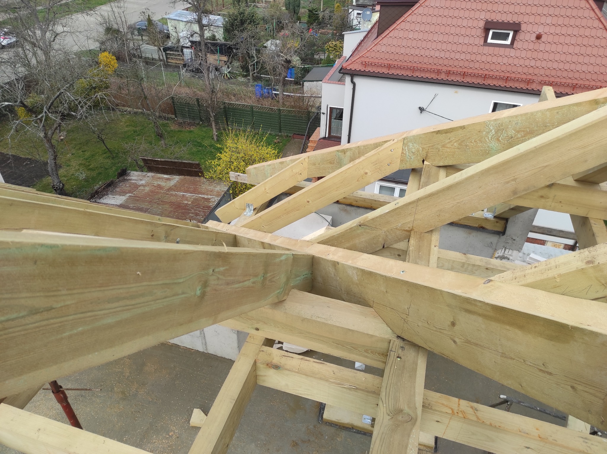 Widok z góry na konstrukcję drewnianą dachu w trakcie budowy, z widocznymi elementami więźby i fragmentami budynku w tle.