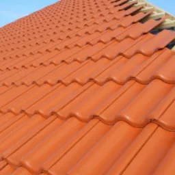 Montaż pomarańczowej dachówki ceramicznej na drewnianej więźbie dachowej, widoczna membrana dachowa i fragment nieba.