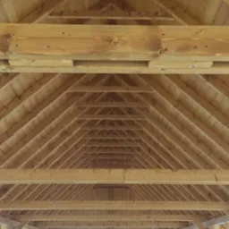 Drewniana konstrukcja dachu z widocznymi belkami nośnymi i krokwiami, jasne drewno, widok od wewnątrz.