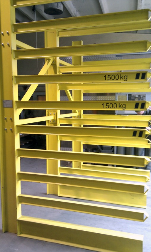 Żółta, metalowa konstrukcja regałowa z poziomymi belkami oznaczonymi jako 1500 kg, widoczna w hali produkcyjnej.