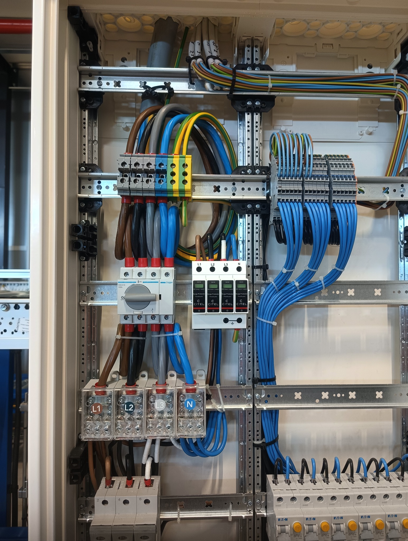 Rozdzielnica elektryczna z zamontowanymi zabezpieczeniami i uporządkowanymi przewodami w kolorach: niebieskim, brązowym, szarym i żółto-zielonym.