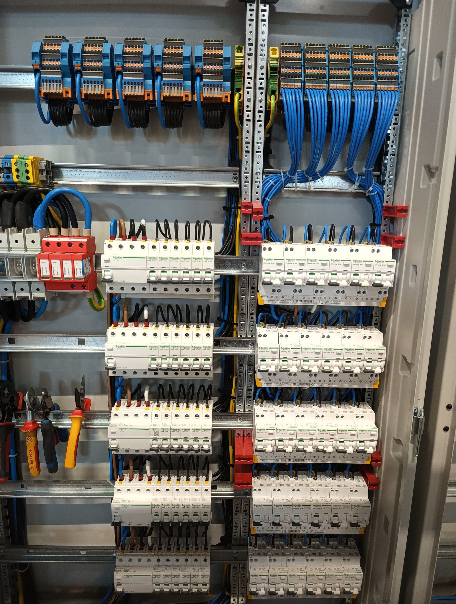 Rozdzielnica elektryczna z zainstalowanymi bezpiecznikami, przewodami w kolorach niebieskim i czarnym, listwami zaciskowymi i narzędziami na boku.